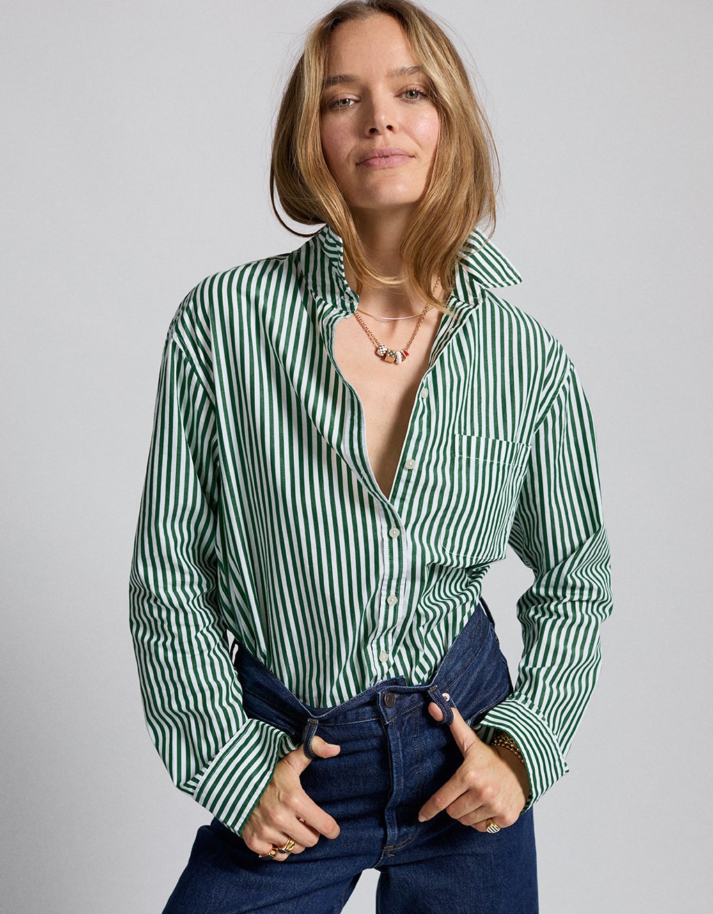 Woman wearing a green and white striped button down shirt with popped collar on a gray background
