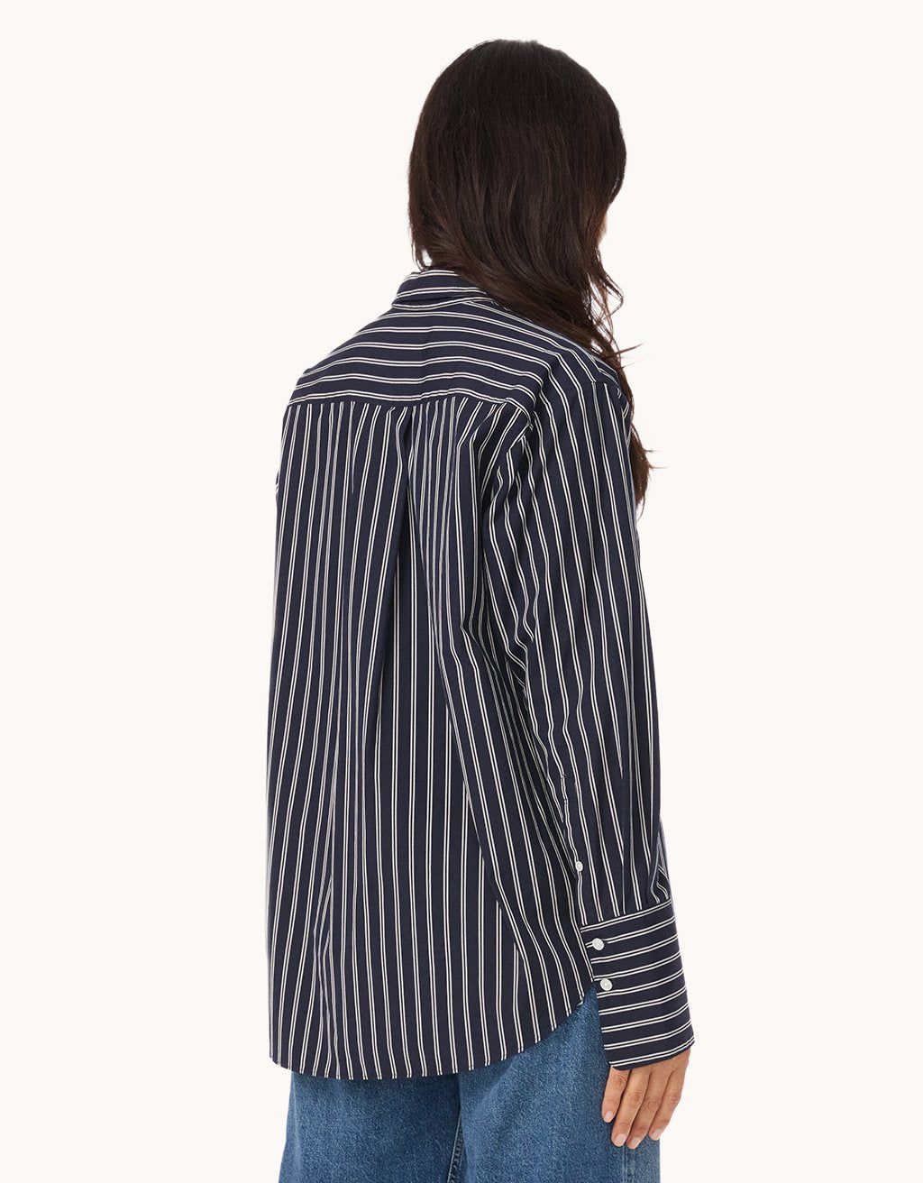 Back view of a person wearing a black and white striped shirt with blue jeans on a white background