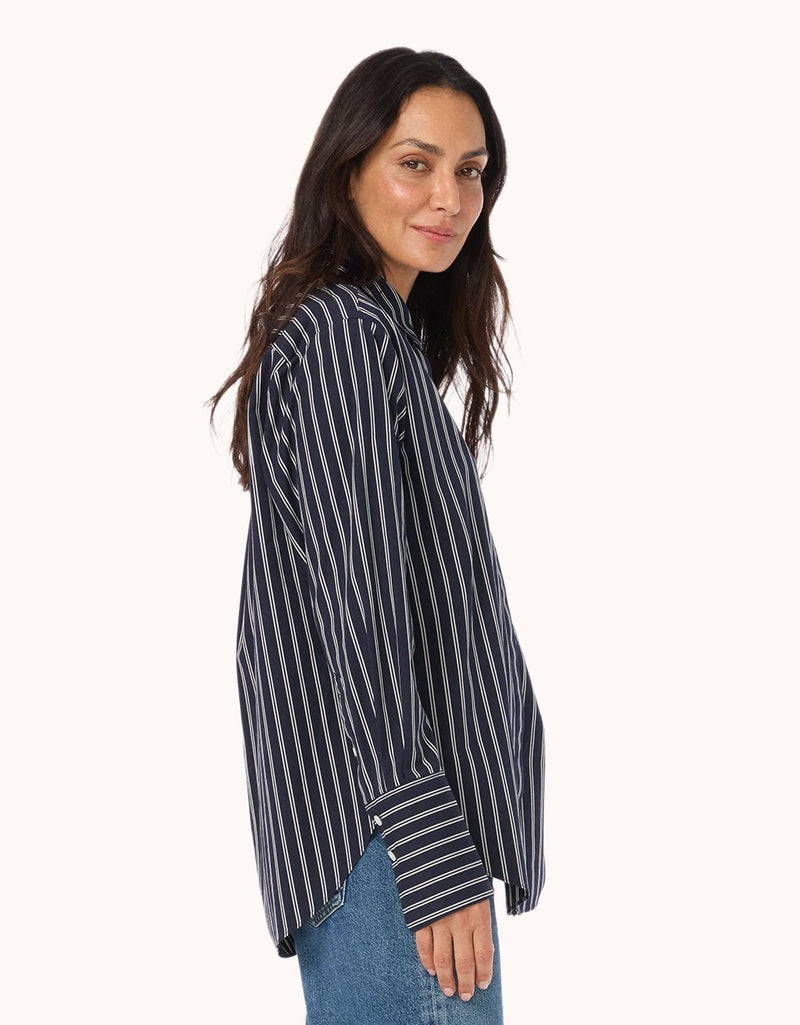 Side view of a woman wearing a black and white striped shirt with blue jeans on a white background