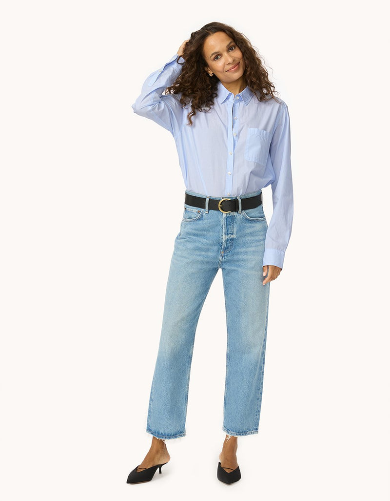 Woman wearing a light blue button down shirt and jeans on a white background