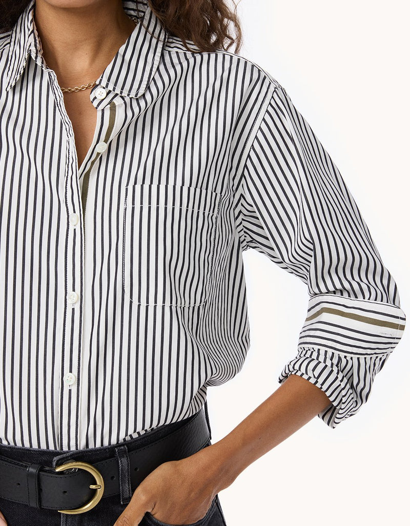 Close-up of a woman wearing a black and white striped button down shirt with black jeans and a black belt on a light gray background