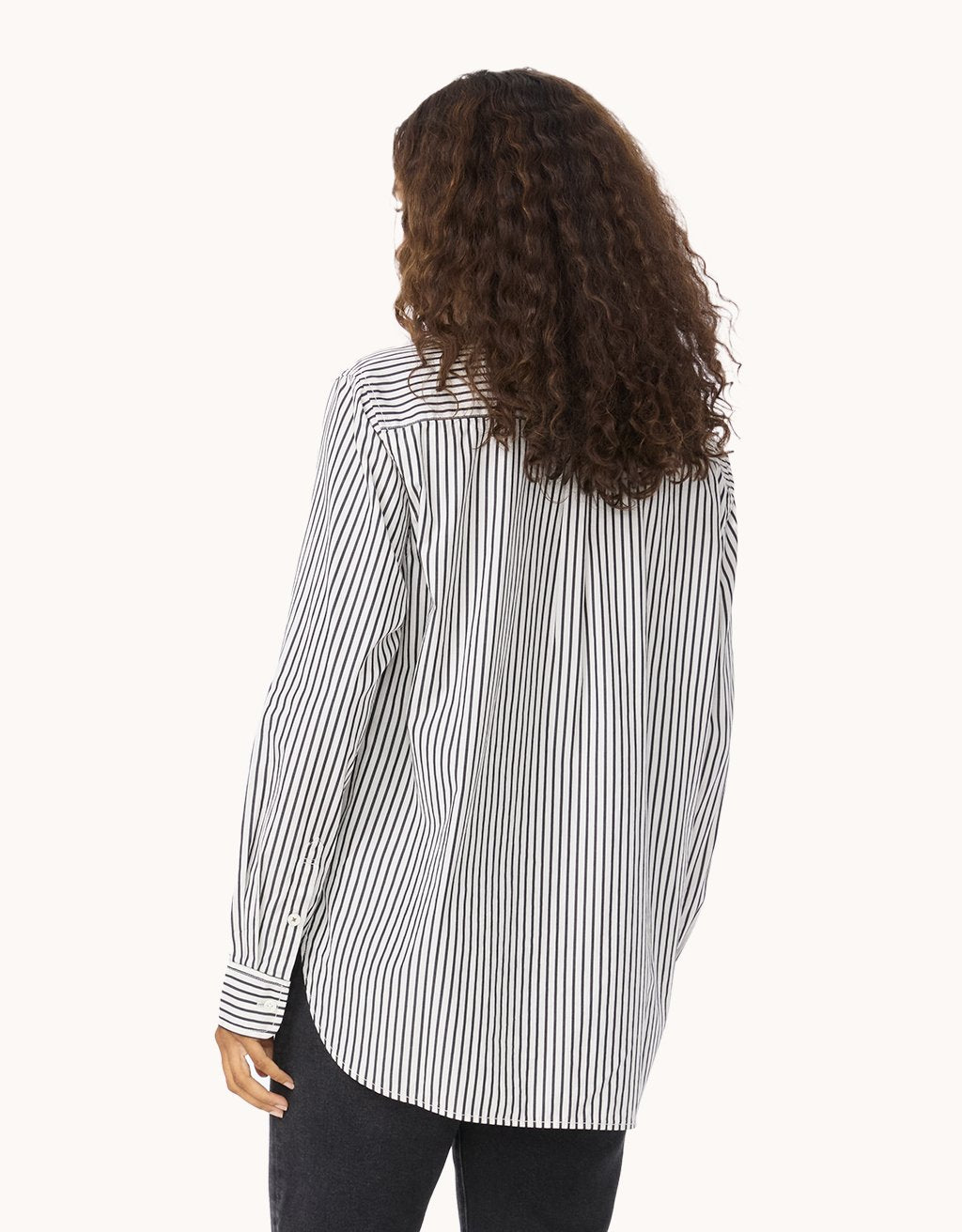 Back view of a woman wearing a black and white stripe shirt with black jeans on a light gray background