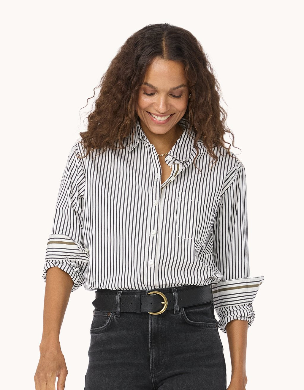 Woman wearing a black and white striped button down shirt with rolled-up sleeves on a light gray background