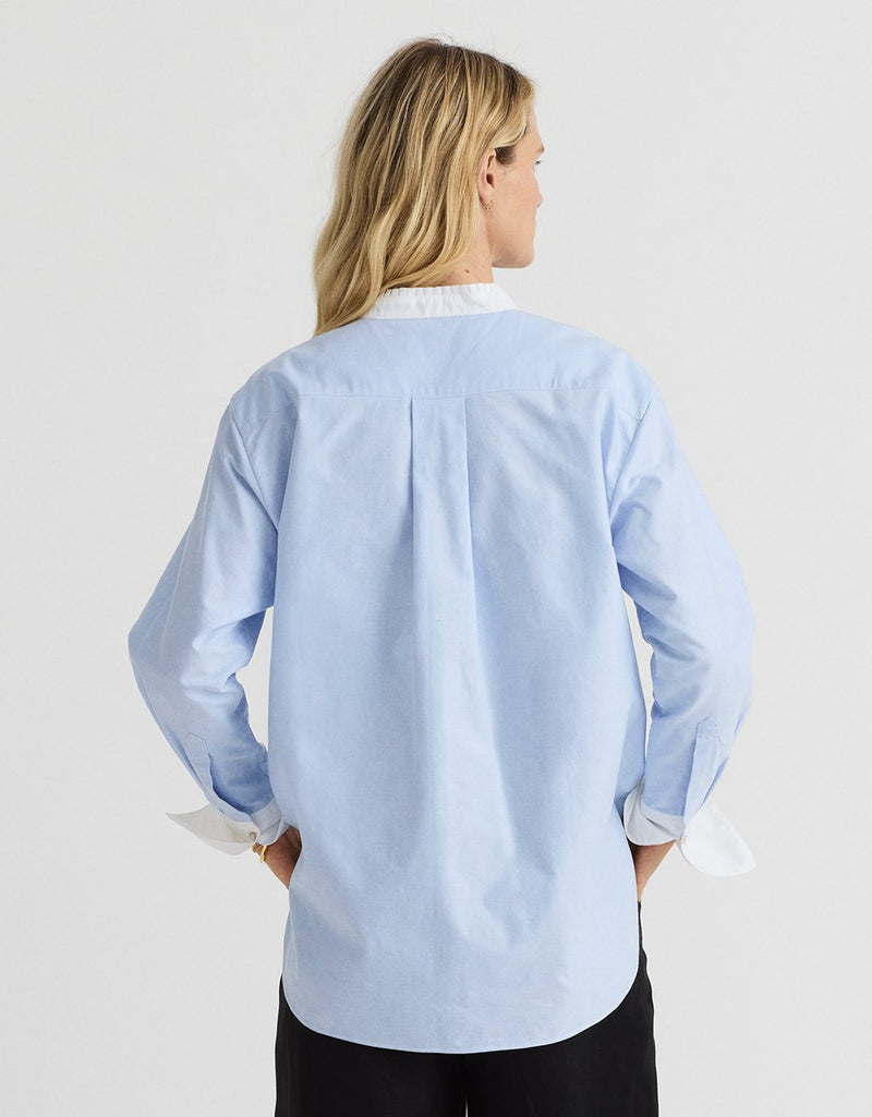 Woman wearing a light blue oxford shirt on a white background