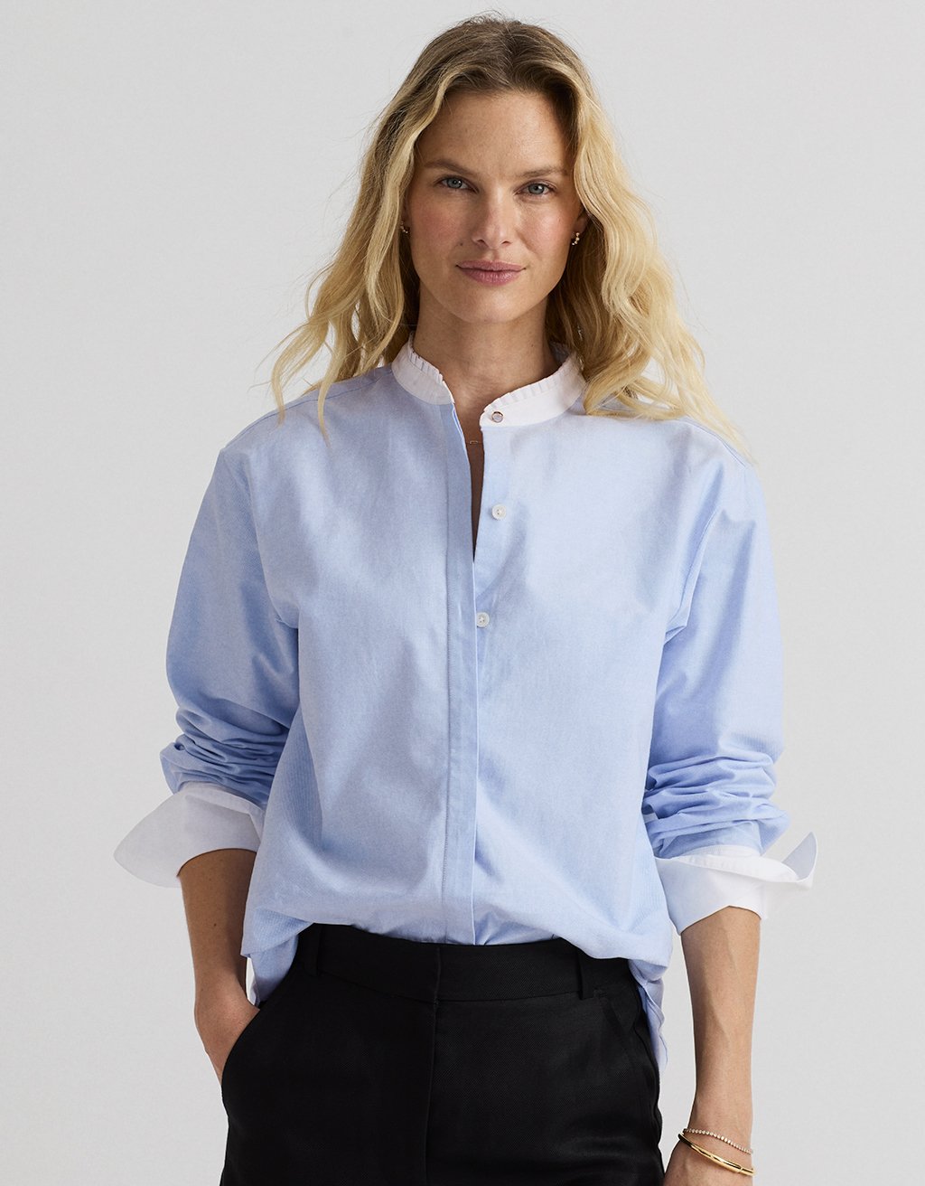 Woman wearing a light blue oxford shirt with contrast rolled-up sleeves on a plain background