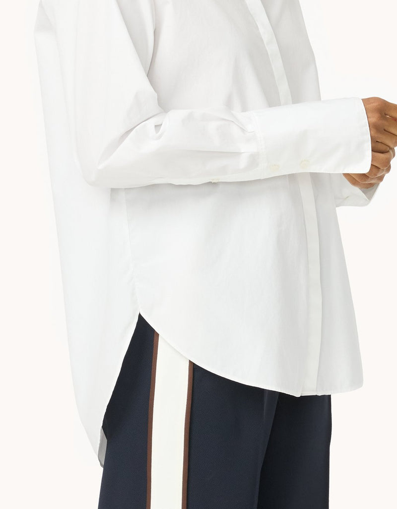 Side view of a person wearing a white blouse with long sleeves and a high-low hemline with navy pants
