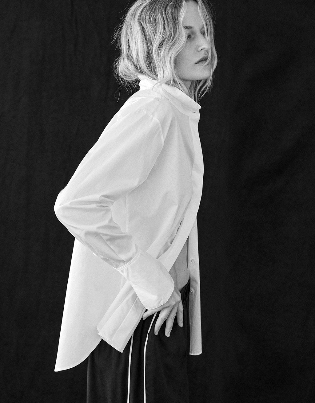 Woman wearing a white button down shirt and multicolor striped skirt sitting against a beige wall.