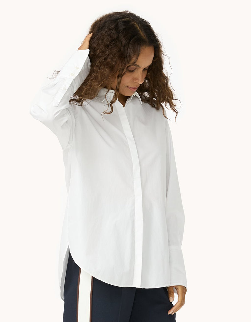 Woman wearing a white button down shirt and navy pants with white side stripe detail on a white background