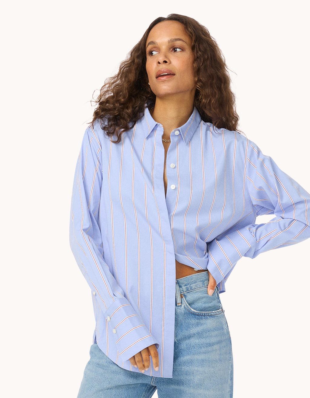 Woman wearing a light blue button down shirt with red and white stripes and blue jeans on a light gray background