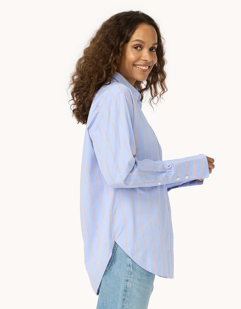 Side view of a woman wearing a light blue button down shirt with red and white stripes on a light gray background
