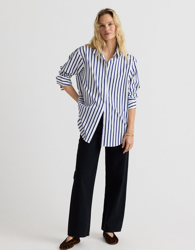 Woman wearing a cobalt blue and white striped button down shirt with black pants on a white background