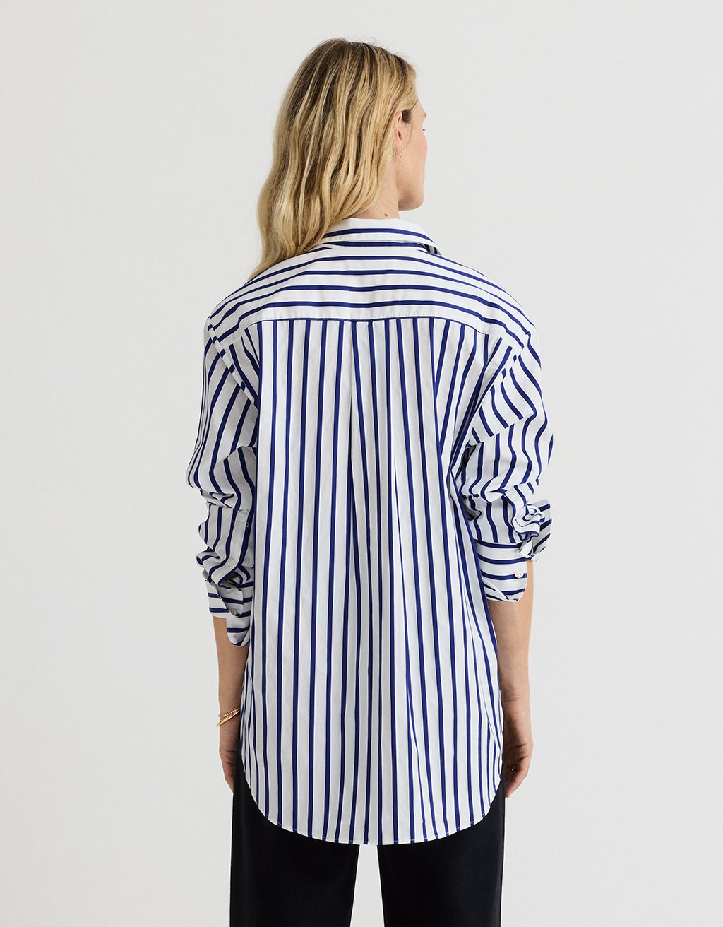 Back view of a woman wearing a cobalt blue and white striped shirt with a rounded hem on a light gray background