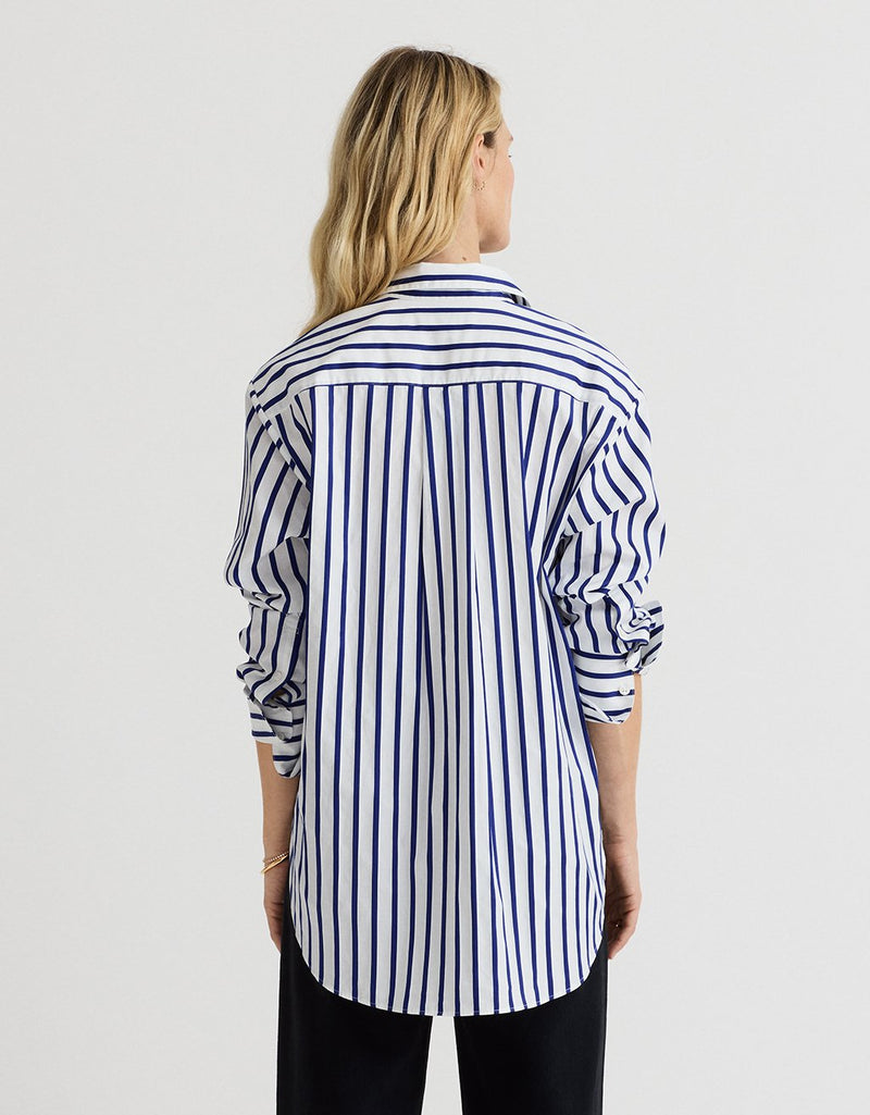 Back view of a woman wearing a cobalt blue and white striped shirt with a rounded hem on a light gray background