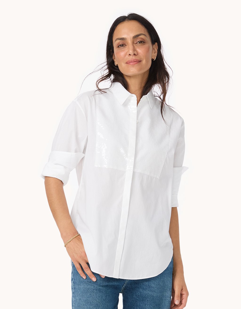 Woman wearing a white button down shirt with sequin bib detail and blue jeans on a white background