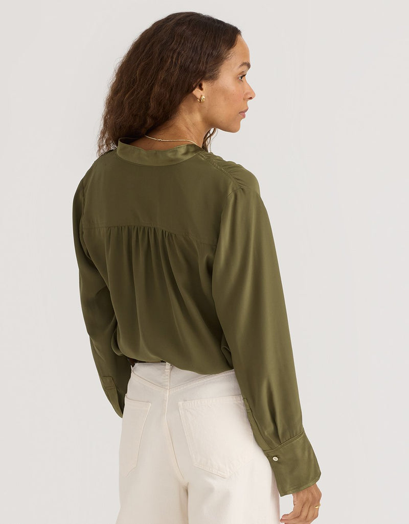 Woman wearing an olive green silk blouse with a plain background