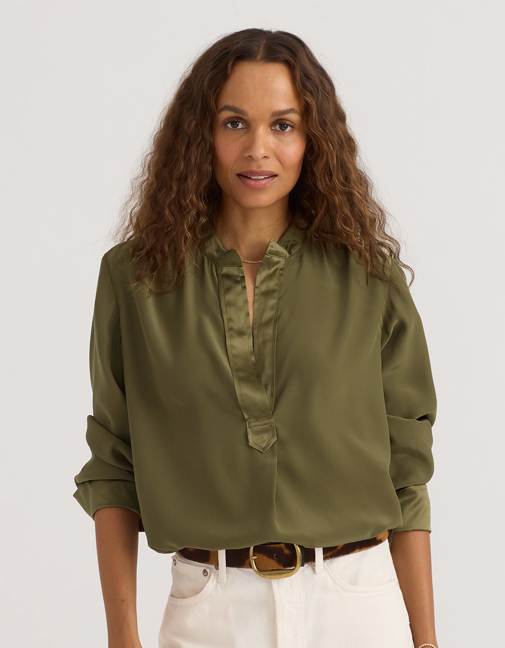 Woman wearing an olive green silk blouse with a plain background