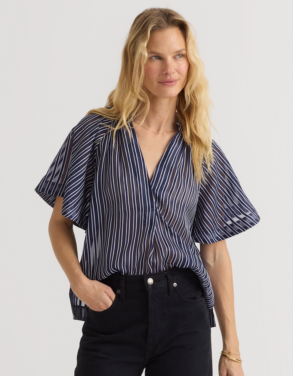 Woman wearing a navy and white striped organza blouse with black jeans on a light gray background