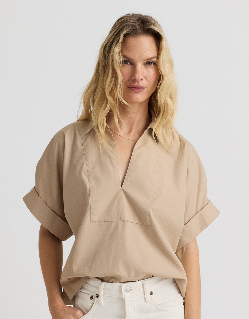 Woman wearing a beige popover blouse with a plain background