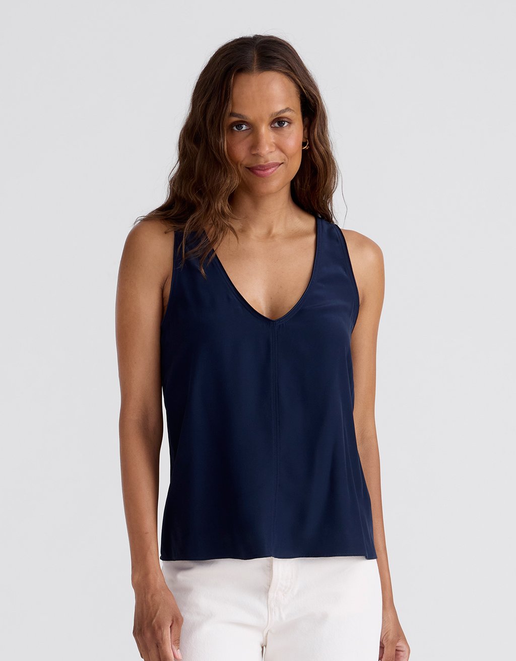 Woman wearing a navy silk tank top with a plunge V-neckline on a white background