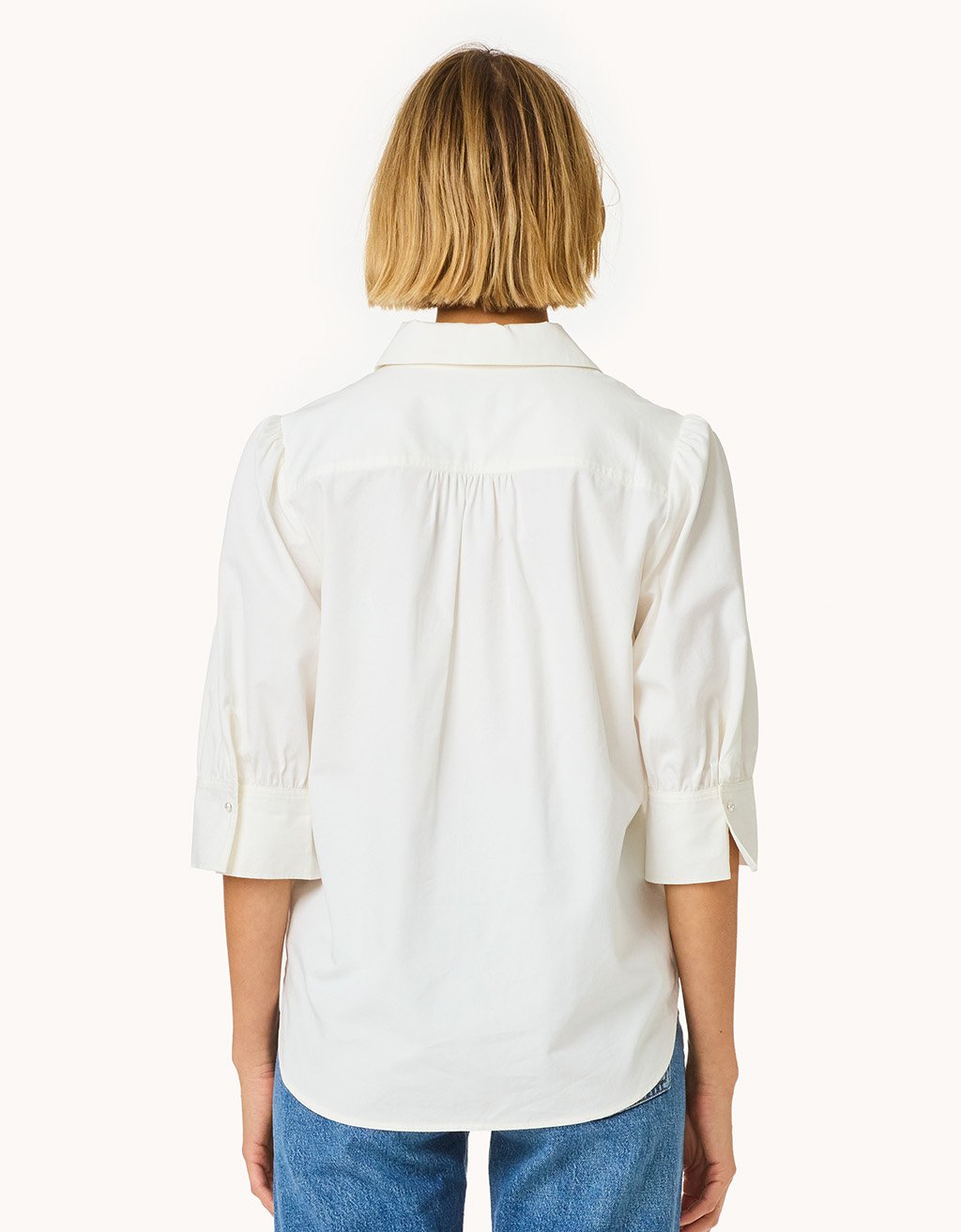 Back view of a woman wearing a white puff sleeve button down shirt on a plain background