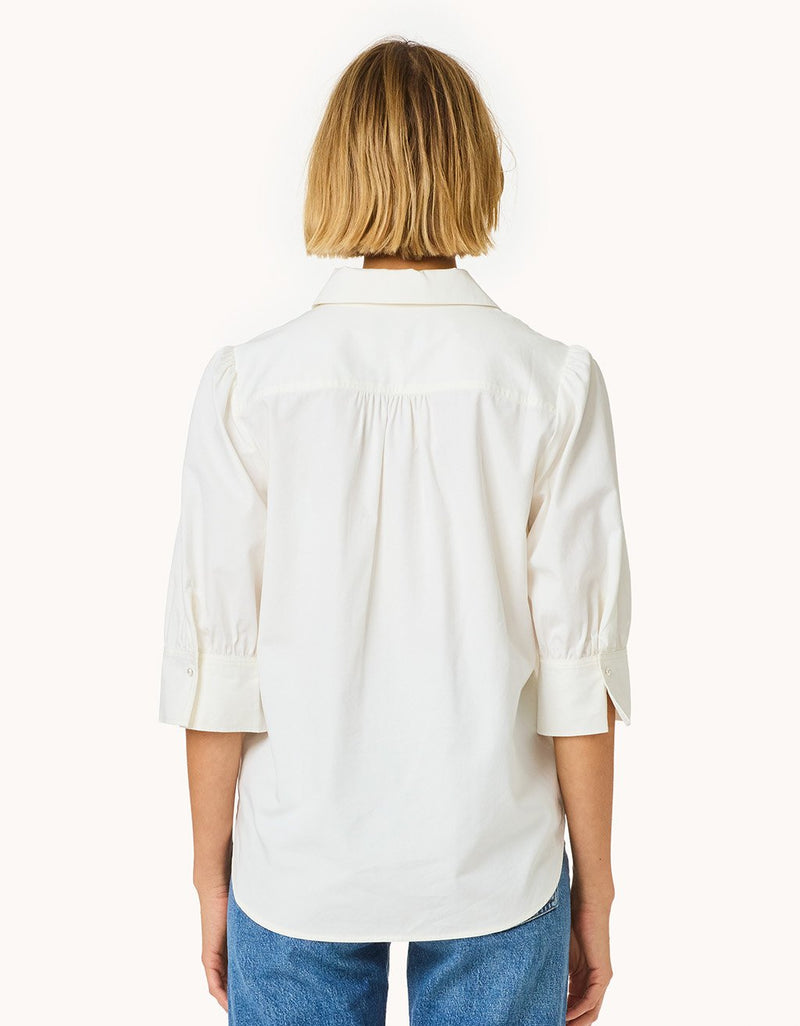 Back view of a woman wearing a white puff sleeve button down shirt on a plain background