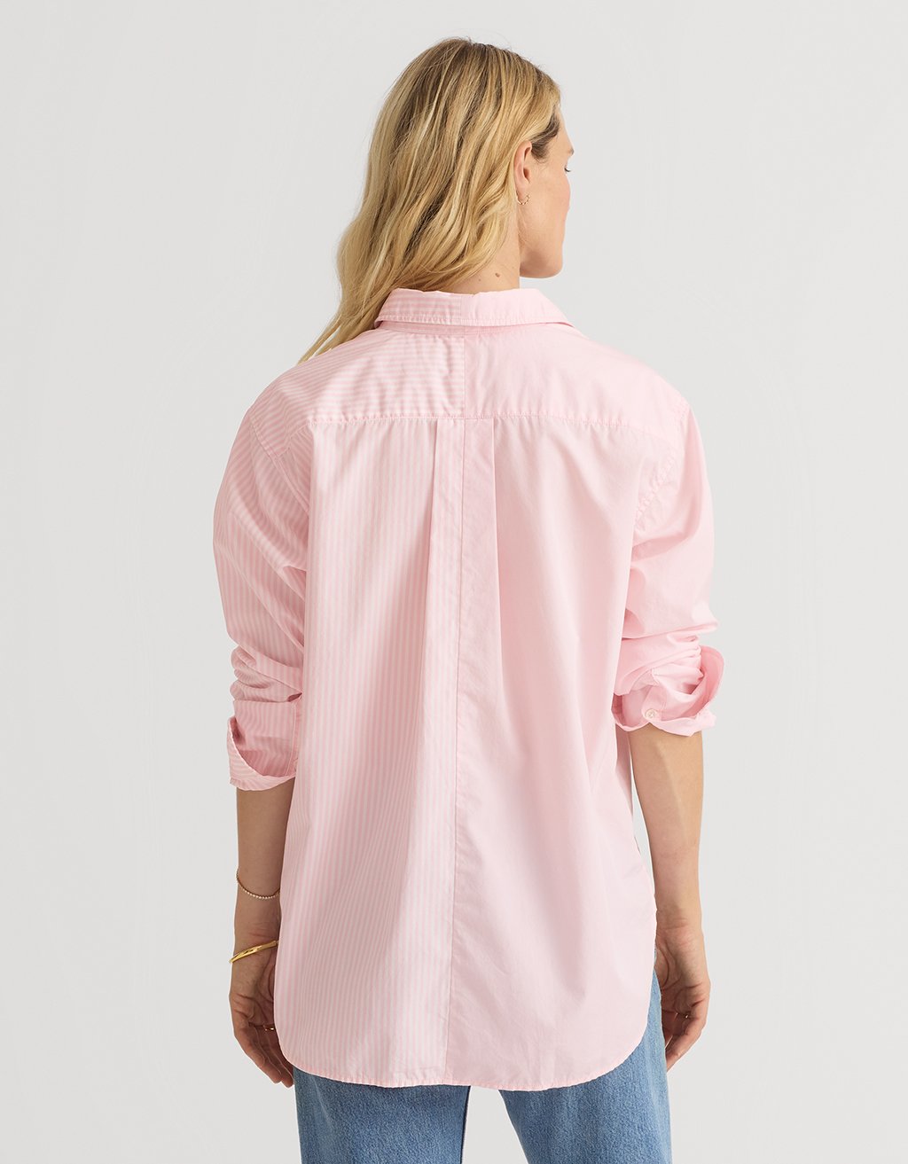 Woman wearing a light pink button down boyfriend shirt and blue jeans on a white background