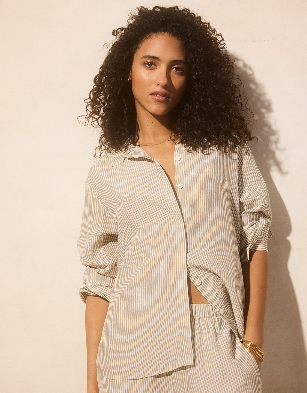 Woman wearing a light-colored striped shirt and pants against a beige background