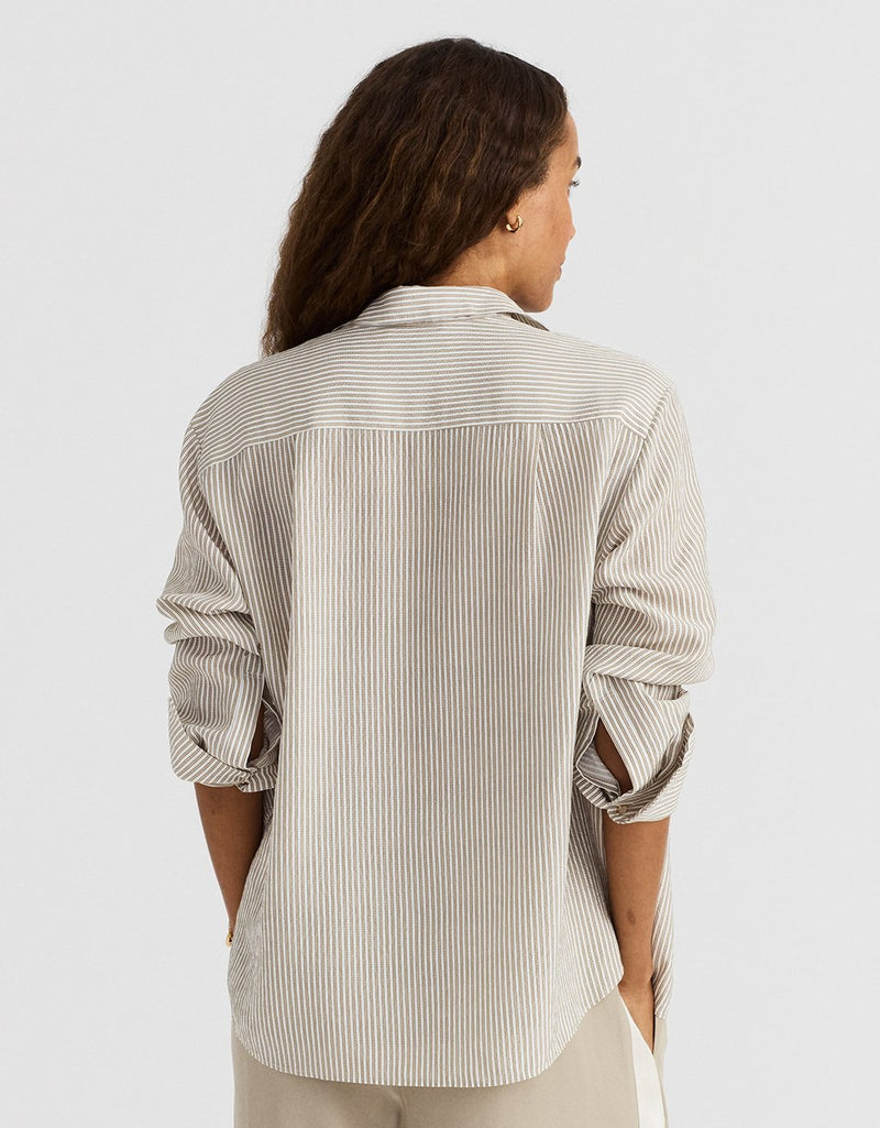 Woman wearing a striped shirt from behind on a light gray background