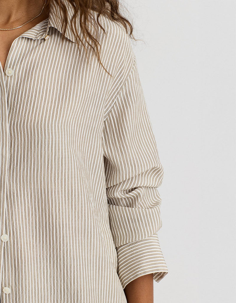 Close-up of a person wearing a beige and white striped shirt on a plain background