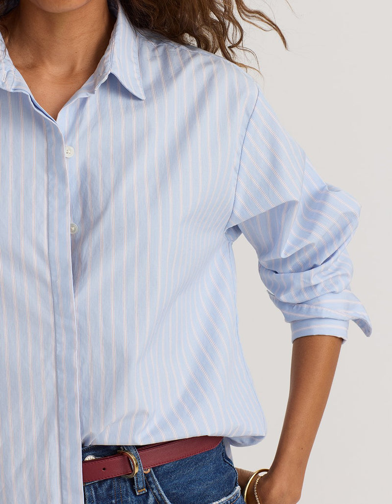 Close-up of a woman wearing a light blue striped boyfriend shirt with rolled-up sleeves.