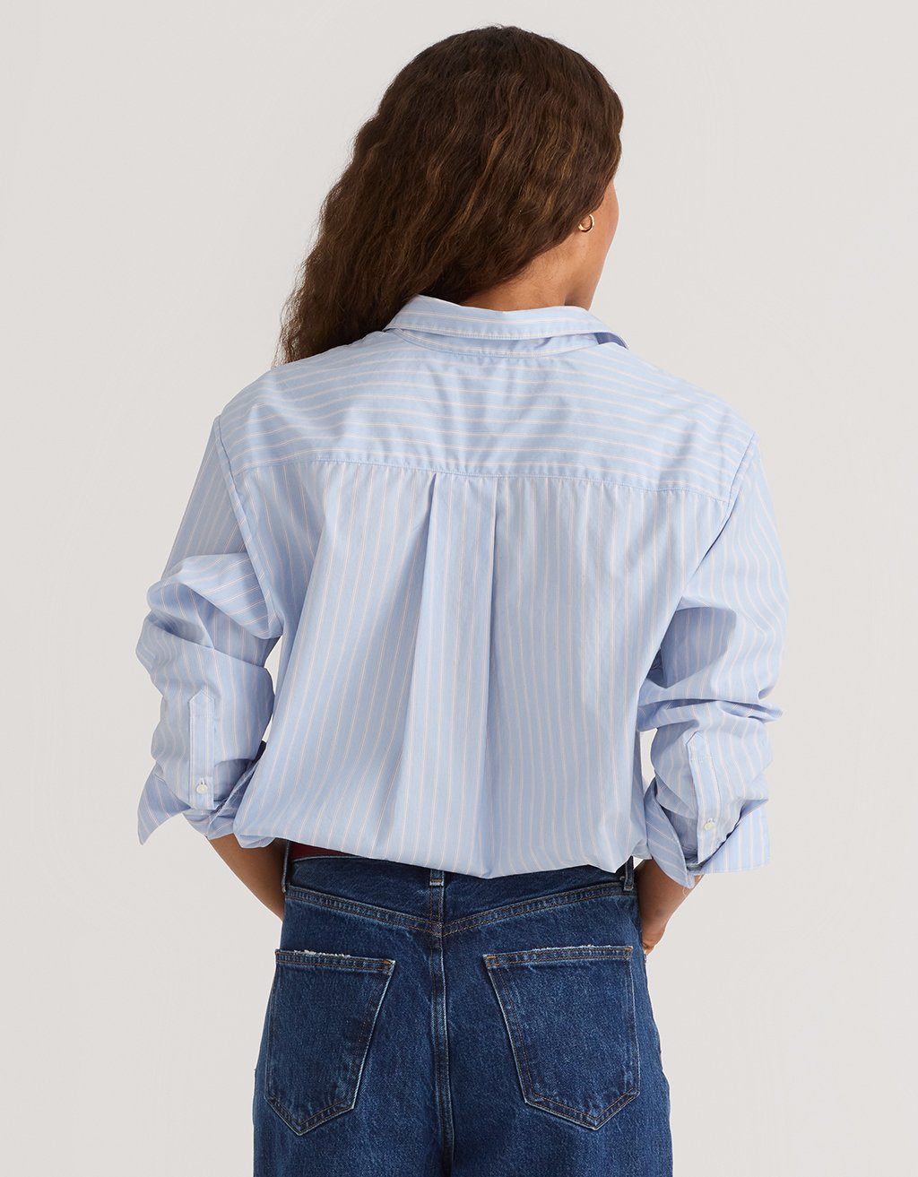 Woman wearing a light blue striped boyfriend shirt and jeans on a plain background