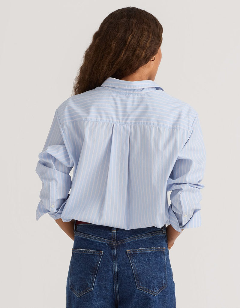 Woman wearing a light blue striped boyfriend shirt and jeans on a plain background