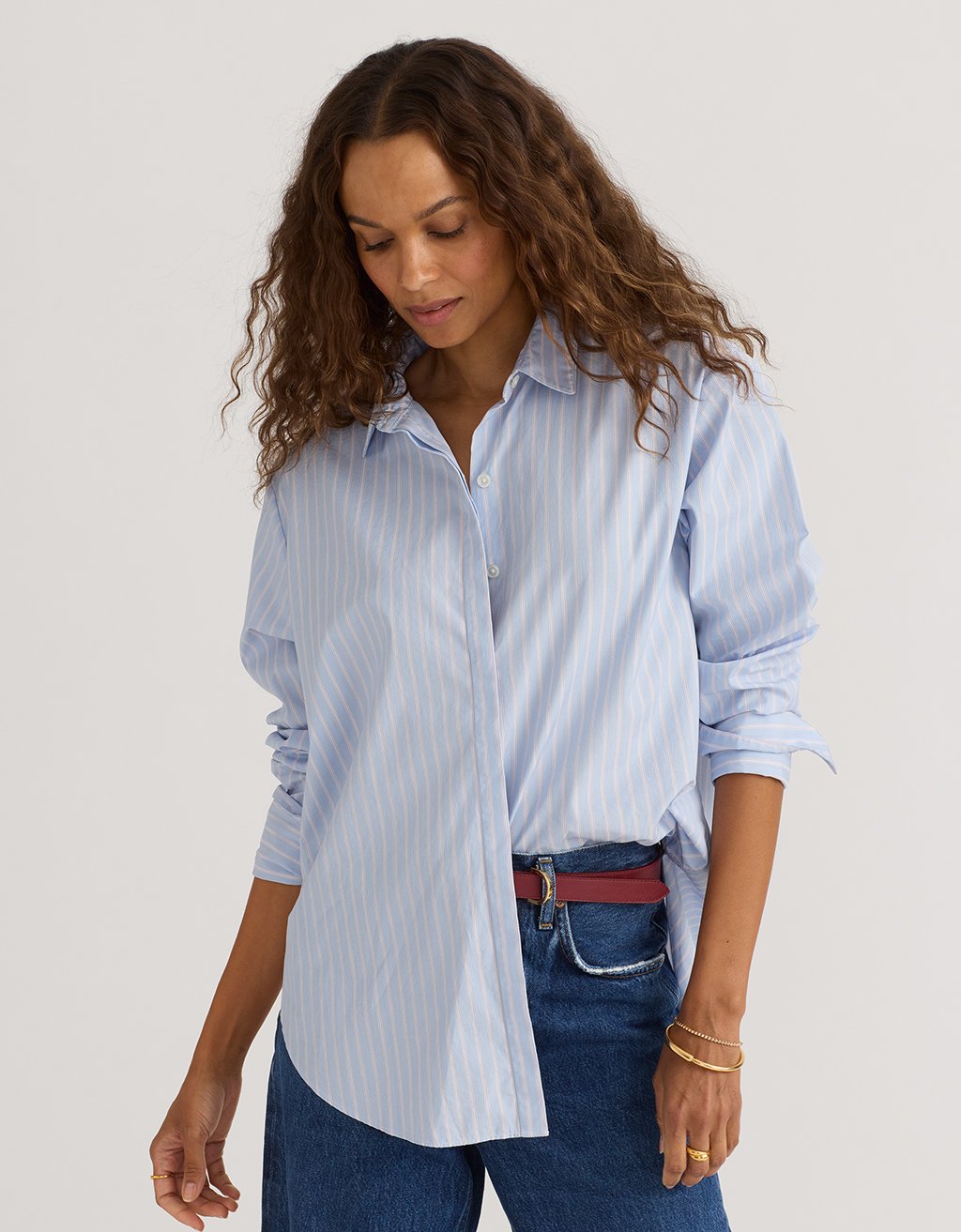 Woman wearing a light blue striped boyfriend shirt and jeans on a plain background