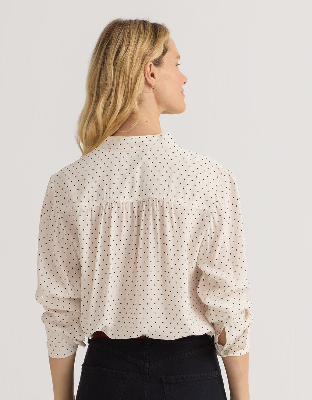 Back-view of a woman wearing a polka dot blouse and black jeans against a plain background