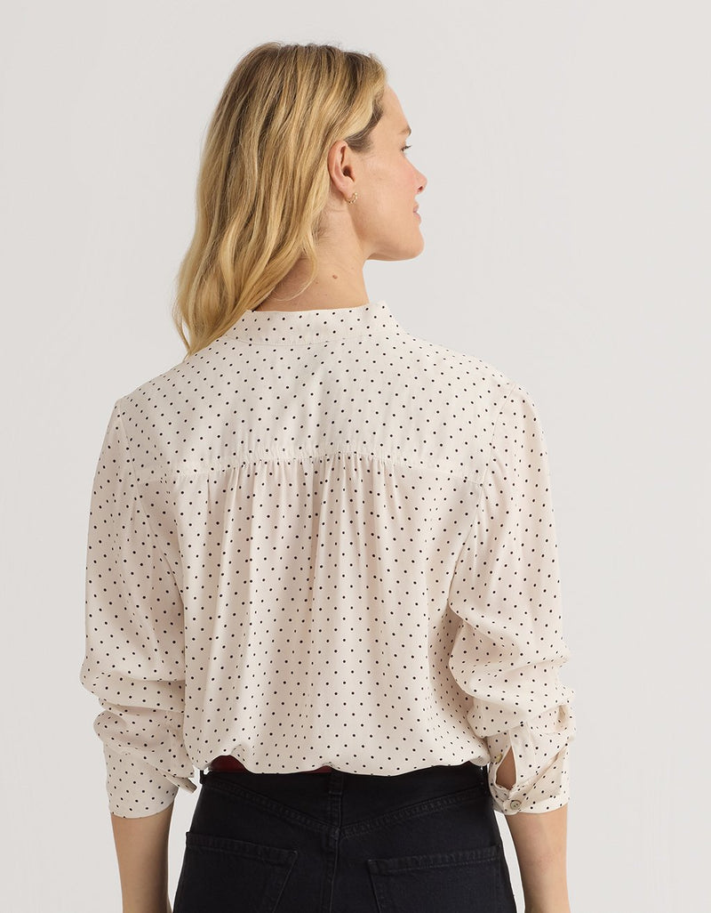 Back-view of a woman wearing a polka dot blouse and black jeans against a plain background