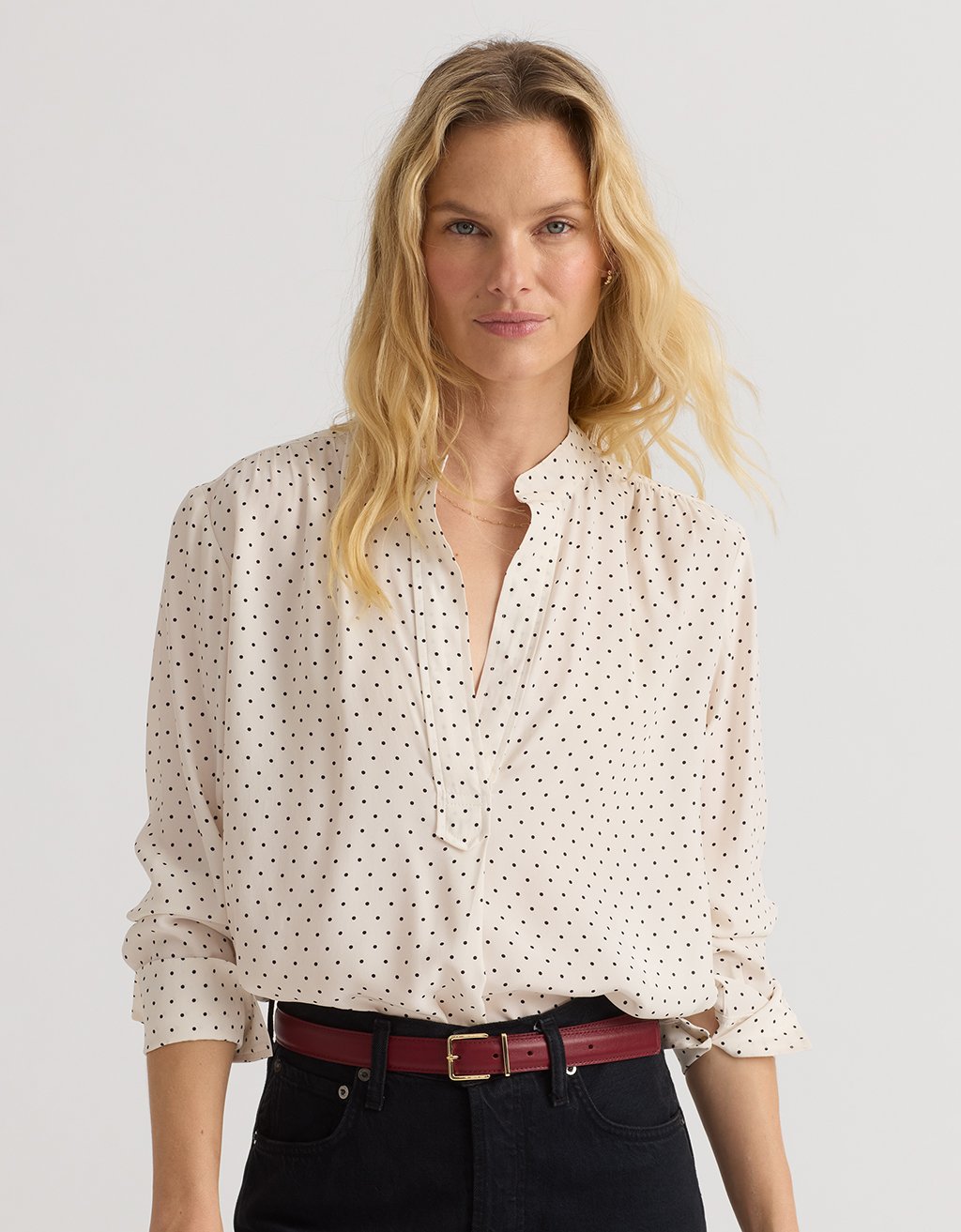 Woman wearing a polka dot blouse, red belt and black jeans with a plain background