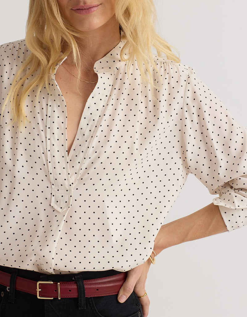 Close-up of a woman wearing a white blouse with black polka dots and a red belt.