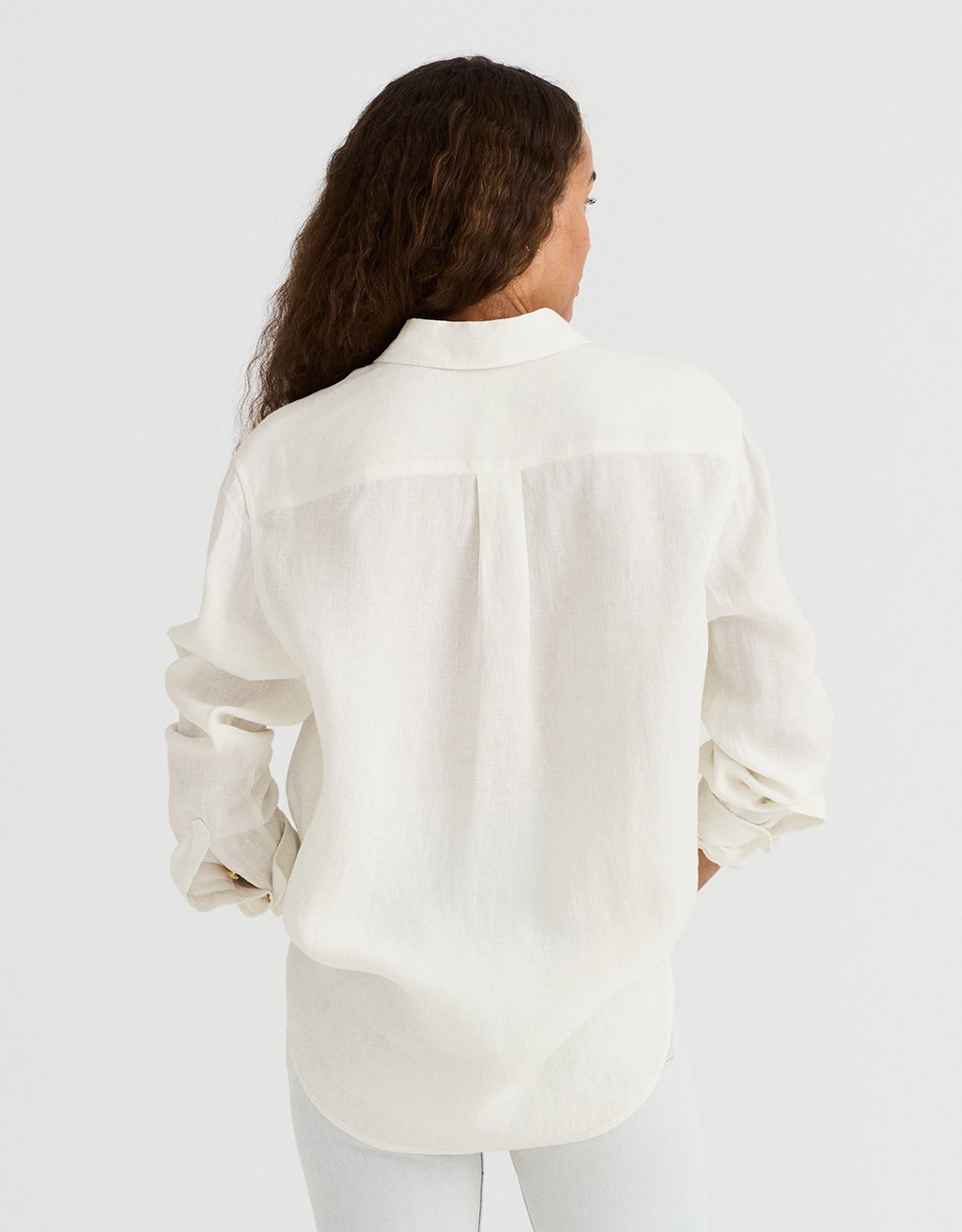 Back view of a woman wearing a white shirt against a plain background