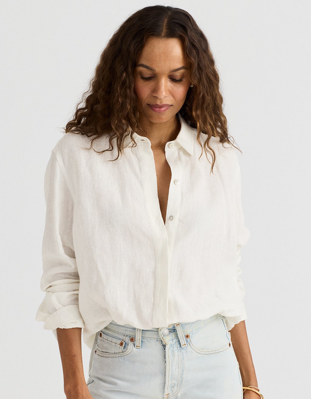 Woman wearing a white button-up blouse and light blue jeans on a plain background