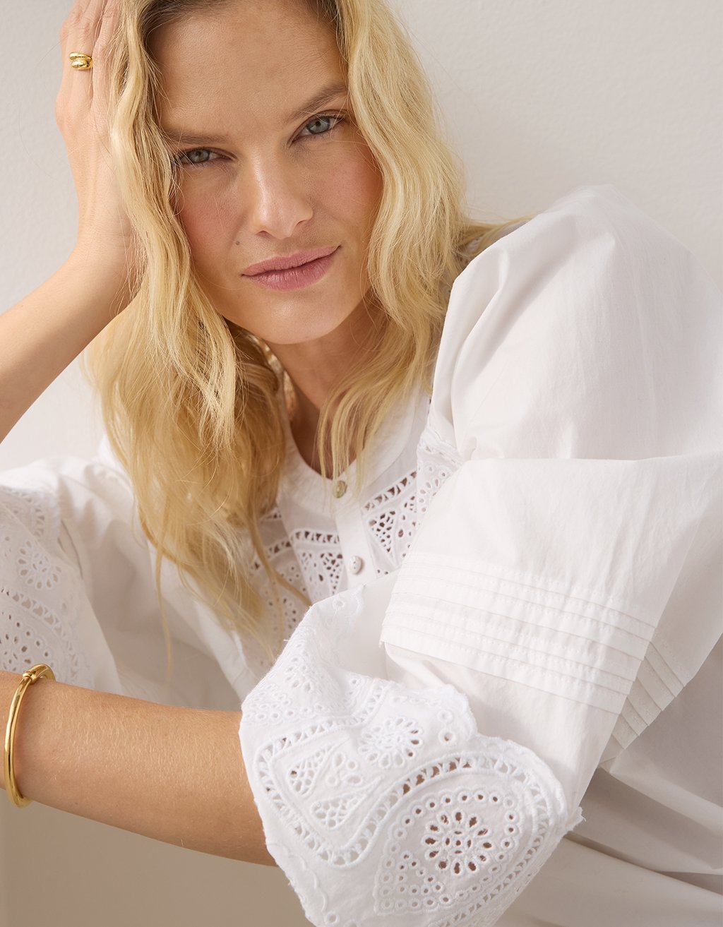 Woman wearing a white poplin blouse with intricate embroidery detailing on a plain background