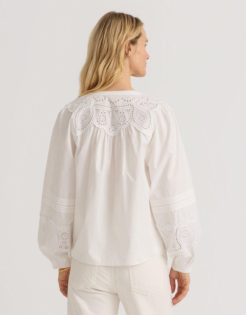 Woman wearing a white poplin blouse with intricate embroidery detailing on a plain background