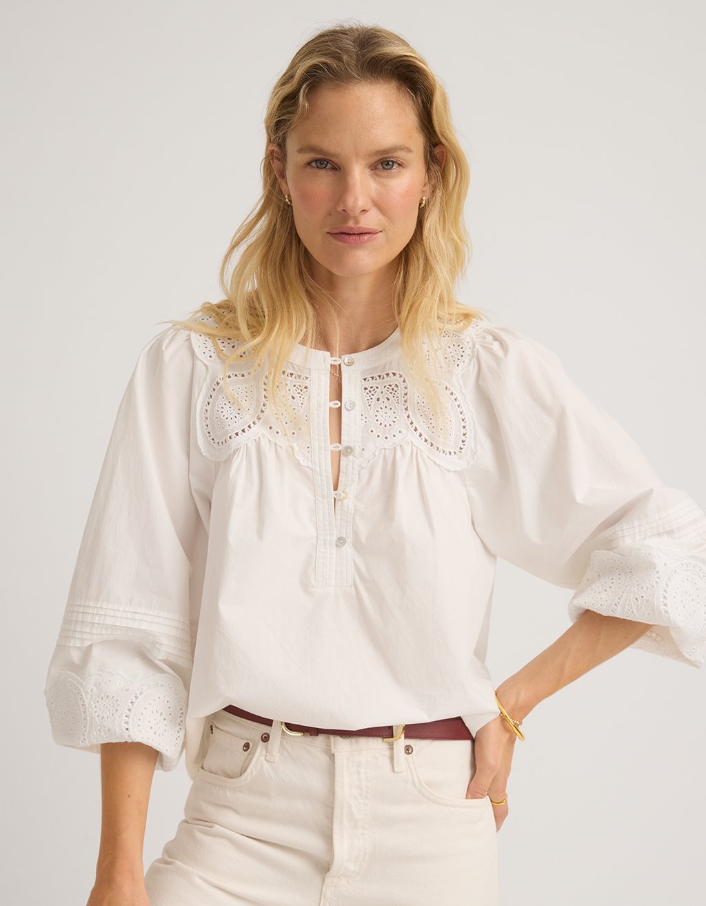 Woman wearing a white embroidered poplin blouse on a plain background