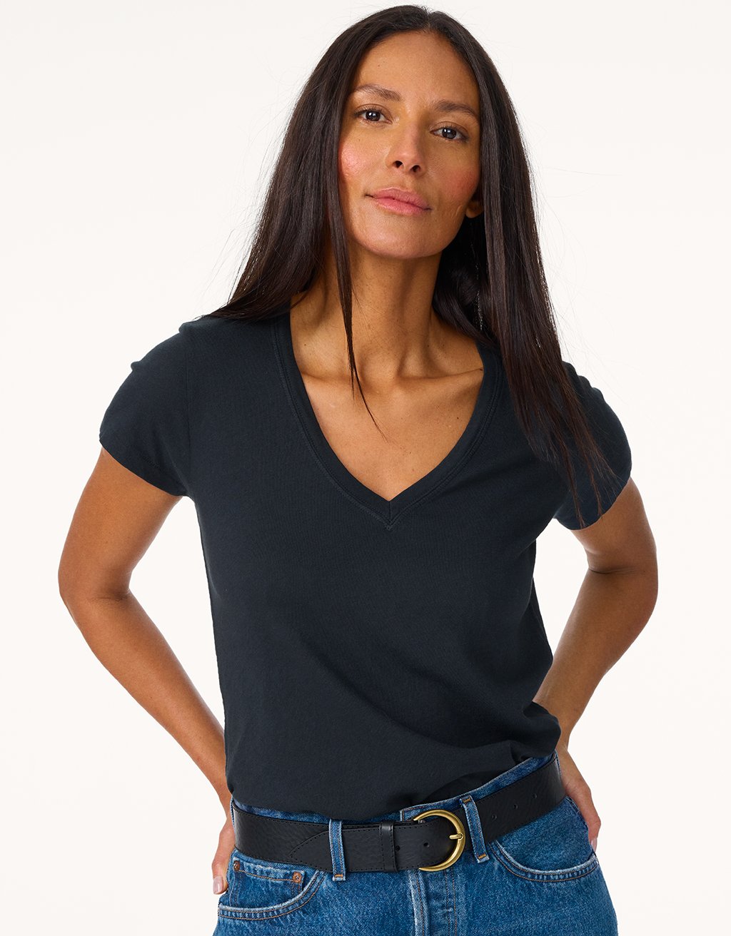 Woman wearing a black V-neck shirt and blue jeans on a light gray background