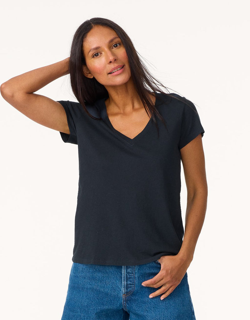Woman wearing a black V-neck t-shirt and blue jeans on a light gray background