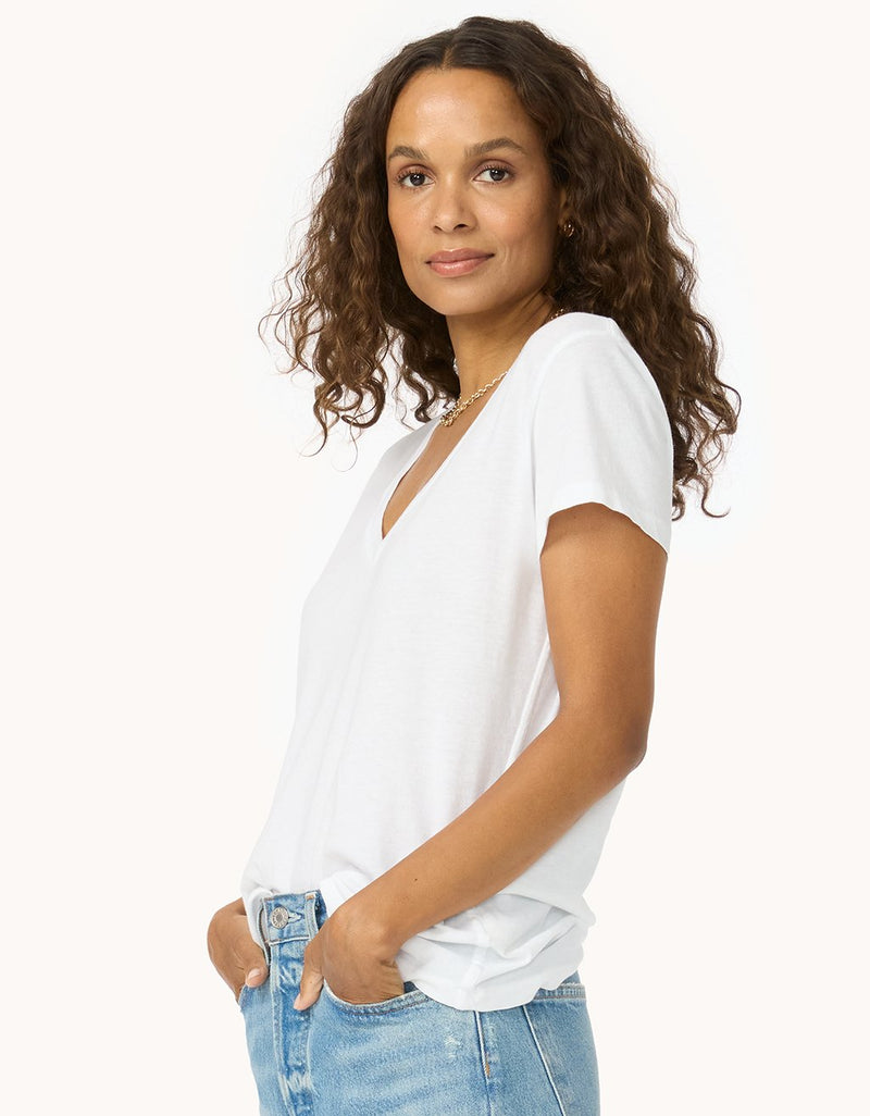 Side view of a woman wearing a white V-neck t-shirt and blue jeans on a white background