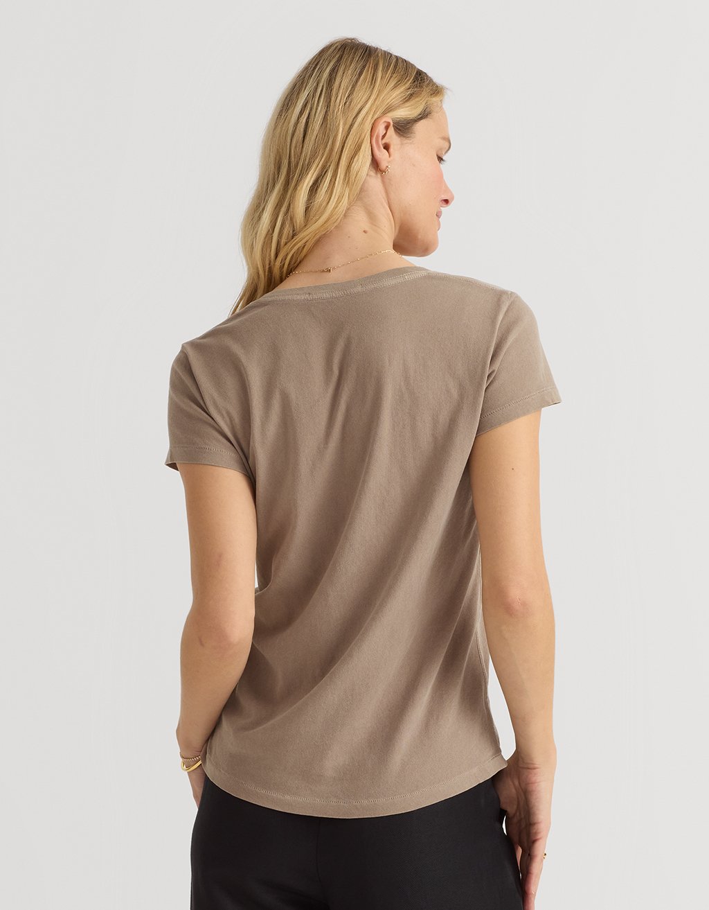 Back view of a woman wearing a beige t-shirt against a plain background