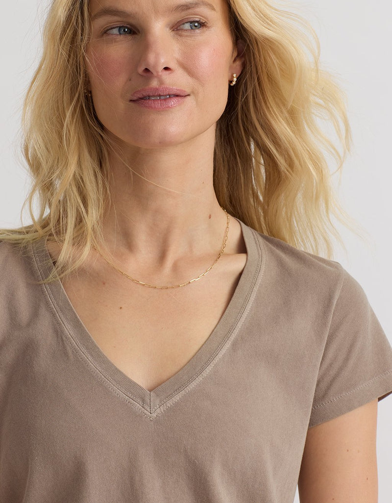 Close-up of a woman wearing a light brown V-neck t-shirt with a plain background