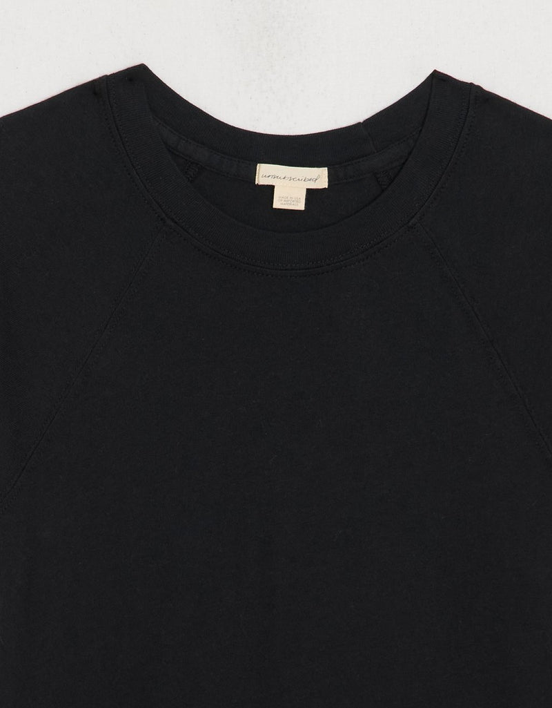 Close-up of a black raglan t-shirt with a visible unsubscribed brand label on a light gray background