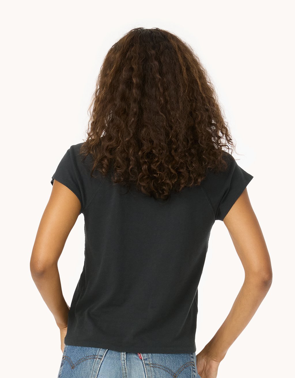 Back view of a woman wearing a black raglan t-shirt and blue jeans on a white background