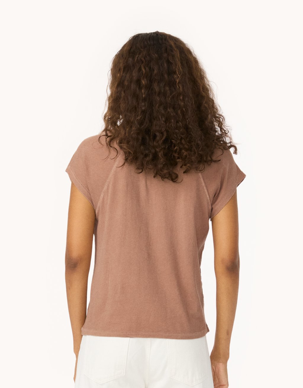 Back view of a woman wearing a cappuccino brown raglan t-shirt and white jeans on a white background